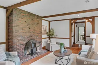 Warm main-level living area with brick fireplace and wood-burning stove, exposed beams, and open flow to the dining room.