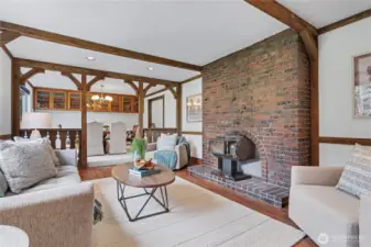 Warm main-level living area with brick fireplace and wood-burning stove, exposed beams, and open flow to the dining room.