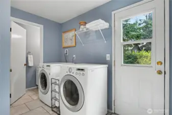 Spacious main-level laundry room and half bath with front-loading appliances, built-in shelving, tile flooring, and direct access to the backyard.