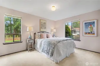 Bright secondary bedroom with large windows, soft wall tones, and views of the surrounding greenery.