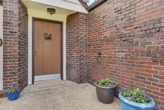 Inviting brick entryway with covered porch, updated exterior lighting, and established plantings framing the front door.