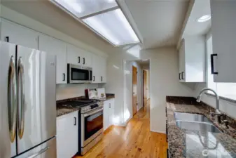 Kitchen with stainless appliances, hardwood floor, looking towards hall to laundry, den/office and garage on the left.