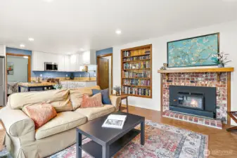 Cozy and inviting, this living area features a charming brick fireplace, custom built-in bookcase, and seamless flow to the full kitchen and dining space—perfect for relaxing evenings or hosting guests in comfort and style.