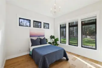 Guest bedroom #1 has views of the lush, green backyard. It offers wood flooring, a chandelier, and a private, ensuite bathroom.