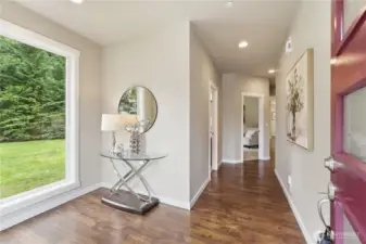A sun-filled entry hall framed by two large windows and grounded by warm laminate hardwood floors