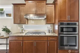 A well-appointed cooking zone featuring a 5-burner gas range, wall microwave, conventional oven, and a stylish Zephyr hood