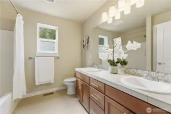 A bright upstairs full bath featuring a double vanity, generous storage, and a fresh, well-kept bath/shower combo.