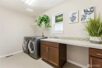 A spacious laundry and utility room with cabinetry, a convenient sink, and newer washer and dryer - a bright, practical workspace.