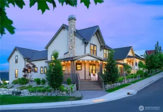 Exterior twilight view of home with classic covered front porch and French doors on a corner homesite.