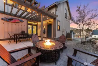 Exterior twilight view of outdoor living space with fire pit, Adirondack chairs and dining table.