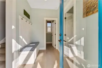 Entryway from side patio door with French Doors and built-in bench with powder room straight ahead and the main floor Primary bedroom to the right.