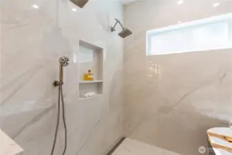 Spacious luxury shower featuring a rain shower head and handheld wand, stunning white interior, heated floors, and a massive window flooding the space with natural light.