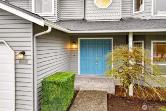 A bold teal double entry door framed by classic coach lighting and manicured boxwood hedging makes a memorable first impression — this is an entrance designed to welcome you home in style every single day.