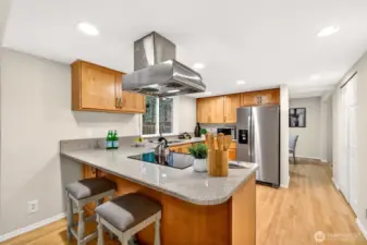 The peninsula with bar seating creates a natural hub for casual meals and conversation, while the cooktop with overhead vent hood and quartz counters bring both style and serious cooking capability to this well-appointed kitchen.