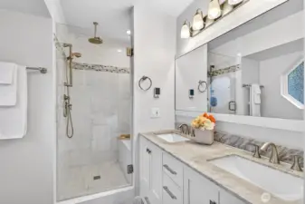 The beautifully remodeled primary bath is a standout feature of this home, showcasing a frameless glass shower with tile surround, rain head fixture, dual undermount sinks with marble countertops, and heated floors — a spa-quality upgrade that transforms the daily routine into something you look forward to.