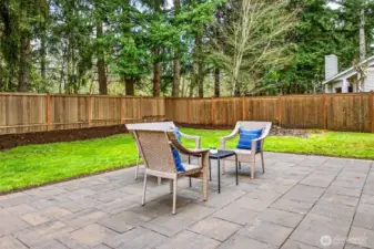 The spacious paver patio offers a private outdoor living space wrapped in the sights and sounds of the Pacific Northwest, with a fully fenced yard, lush lawn, and a towering backdrop of mature evergreens that create a natural sense of seclusion and serenity.