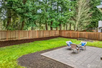 The fully fenced backyard on this nearly 8,750 square foot lot provides an impressive amount of usable outdoor space — a paver patio anchored by the home, generous lawn area, fresh mulched beds, and a natural evergreen buffer that creates true privacy year round.
