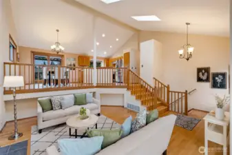 Open and airy main living space with soaring ceilings, skylights, and a bright upper-level dining area overlooking the living room. Natural light pours through large windows, creating a cheerful, connected atmosphere.