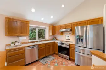 A bright, cheerful kitchen with vaulted ceilings, stainless steel appliances, and a wide window over the sink offering views of the greenery outside. Thoughtful updates blend seamlessly with timeless finishes.
