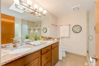 Beautifully remodeled ensuite bath featuring a dual-sink vanity with granite counters, modern lighting, and a walk-in shower with tile surround and glass enclosure.