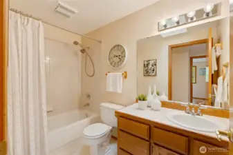 Bright and clean full bath with a tiled shower and tub combo, wood vanity, and modern fixtures. A large mirror and warm lighting make the space feel open and inviting.