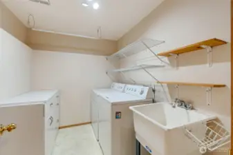 Convenient laundry room with full-size washer and dryer, deep utility sink, built-in shelving, and additional cabinetry for storage and organization.