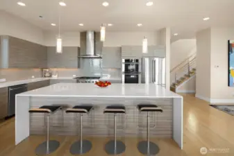 An expansive waterfall white quartz island counter invites guests to join the party while leaving plenty of space for the chef to work their magic