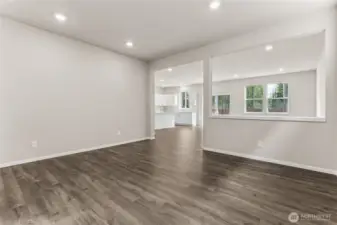 Open-concept great room with hardwood floors, neutral walls, recessed lighting, and a large window with natural backyard views, with an open sightline to the kitchen beyond. Photos are representative only and may display different color packages and/or upgrades.