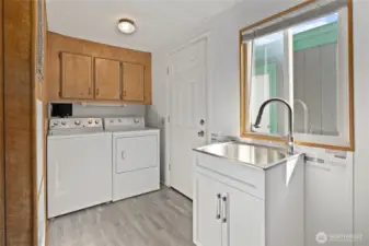 Utility room with built in large sink vanity new flooring and new windows, access out to the backyard and garage.