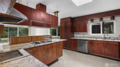 Kitchen features stainless steel appliances, terrazzo floors, warm cabinetry, and window above the sink.