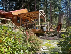 Wonderful Pan Abode cedar home with many features. Here is the covered pavilion area - great area all year around! Notice the wood carving in the tree stump beside the deck.
