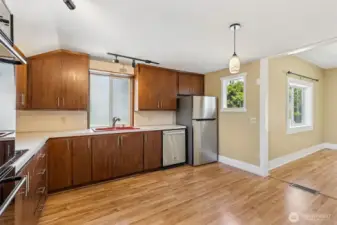Unit A’s kitchen is designed with both style and function in mind. Stainless steel appliances and dark coffee-tone modern flat-front cabinetry with sleek stainless hardware create a contemporary look. The warm wood laminate floors add richness, and the red sink in front of the window is a bold, eye-catching detail. With double ovens in the wall cabinet and a glass-top range cooktop in front of another window, cooking is a breeze. Plus, the spacious layout leaves room to add a center island or an eating dining table, giving you endless possibilities.