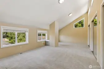 Upstairs in Unit A, this massive vaulted room is a blank canvas for whatever you envision. With oatmeal carpeting and warm-toned walls, it’s a cozy yet spacious area. A big window with wide slat blinds, along with an upper accent window in the vaulted area, fills the room with light. Three huge walk-in closets give you all the storage you need, and the space is large enough to fit multiple sleeping dorm-style bunks or serve as a massive rec room for gatherings. At the end of the upstairs room in Unit A, the open loft space overlooks the staircase, adding a sense of openness and light. A deep walk-in closet at the top of the staircase offers extra storage, while the carpeted stairs ensure safety, comfort, and a quieter feel. The mirrored closet door reflects light, making the space feel even more spacious and bright.