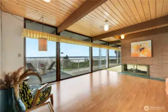 This stunning dining room opens directly to the deck, offering unobstructed views of Puget Sound and the Olympic Mountains. Floor-to-ceiling windows frame the ever-changing landscape, from tranquil water vistas to vibrant, unforgettable sunsets. Warm wood-beam ceilings and a sleek fireplace create an inviting backdrop, while the seamless indoor-outdoor flow makes this an exceptional setting for everyday meals or sunset-lit entertaining. A truly breathtaking space that celebrates Northwest living.