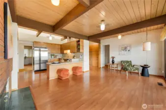 This inviting open-concept living area showcases warm wood-beam ceilings, skylights that pour in natural light, and a seamless flow between the kitchen and living spaces. The kitchen features sleek cabinetry, stainless appliances, and a stylish island with vibrant seating, while the adjacent living area offers comfortable gathering zones and a cozy fireplace. A rare original built-in grill/BBQ adds character and functionality, creating a unique focal point for cooking and entertaining. A bright, welcoming hub designed for everyday living with a touch of nostalgic charm.