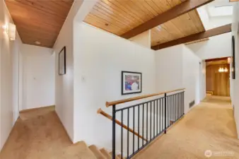 This inviting hallway leads to the finished basement and is brightened by overhead skylights that fill the space with natural light. Warm wood-beam ceilings, crisp white walls, and a modern railing create a clean, airy feel, while thoughtful architectural details add character throughout. A welcoming transition space that enhances the home’s flow and showcases its timeless design.