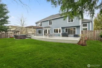 Standing in a corner of the yard looking at the back of the house illustrating the size of the deck and the pergola, and hot tub (that stays).