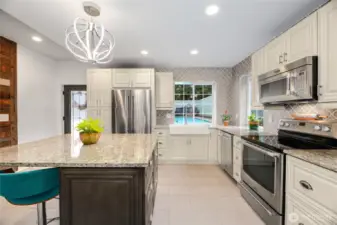 Enjoy a view of the pool while standing in front of the farmhouse sink in this luxury kitchen. Updated with granite counters, a large island with seating and storage, stainless steel appliances, seperate beverage refrigerator, updated lighting.