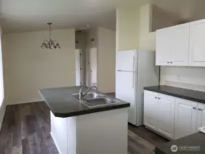 An Opposite Look at the Island Kitchen from the Utility Room showing Dining Room View with White Cabinets and Appliances. New LED Lighting, Newer Counter Tops and Vinyl Plank Flooring.