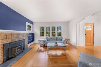 A warm and welcoming living space, this room is bathed in natural light from expansive windows. Featuring a brick wood-burning stove, built-in shelving, and a classic wood door, this is a perfect setting for cozy evenings or entertaining in a bright and stylish atmosphere.