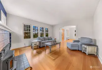 With its beautiful hardwood floors, abundant natural light, and comfortable furnishings, this living room offers a versatile space for both relaxation and entertaining. The seamless flow from the wood-burning stove to the arched doorway creates a harmonious design that connects the home’s warmth and character.