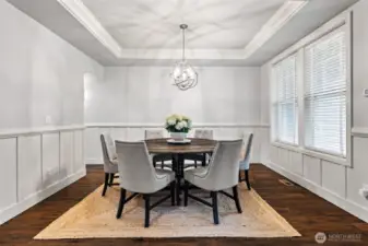 The elegant dining room has a tray ceiling, wainscoting, hardwood floors, and plenty of space to entertain all your guests.