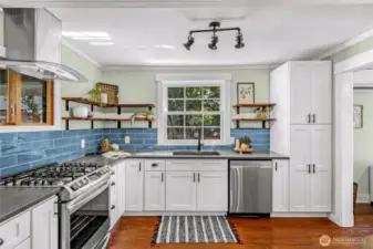 Modern kitchen with quartz counters, ceramic tile back splash, stainless steel appliances, and reclaimed wood open shelving.