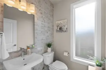 The main level powder room is a stunning showcase of thoughtful design, highlighted by the filtered light that gently streams through frosted glass, creating a soft and inviting ambiance.  The floor to ceiling tiled wall is a beautiful focal point to this well used space.