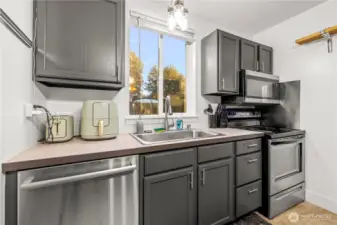 The kitchen is equipped with sleek stainless steel appliances and a dedicated workspace. A window over the sink lets in natural light and provides a pleasant view while you wash dishes.