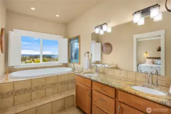 Primary ensuite bath with double vanity, granite countertops, and soaking tub beneath a window capturing beautiful water views.