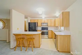 Kitchen with a large peninsula, breakfast bar, lots of cabinet space, black and stainless steel appliances, and a garden window.  Barstools stay!