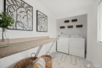 Spacious utility & laundry room with work bench to make folding a breeze. Wire closet racks above washer and dryer for convenient storage. Located right off dining room on primary wing of house. LVP tile flooring for easy cleaning.