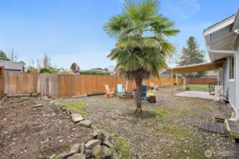 North end of backyard features a large rocked lined raised garden bed, established palm tree and firepit area.