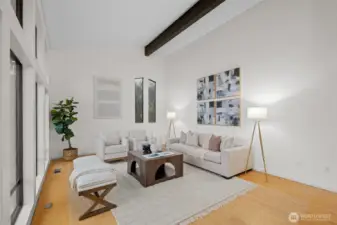 Enjoy entertaining here, or relax with family or spoil your guests in comfort and style. Light colored walls lift the spirit and brighten the space. Two story view windows fill the room with beautiful natural light and look out toward the mountains and the Puget Sound. The soaring ceiling and warm wood floors create an airy, uplifting atmosphere that feels both peaceful and refined. A pair of tall accent windows adds soft, filtered light on the opposite wall, and exposed beams lend the room a timeless architectural charm.